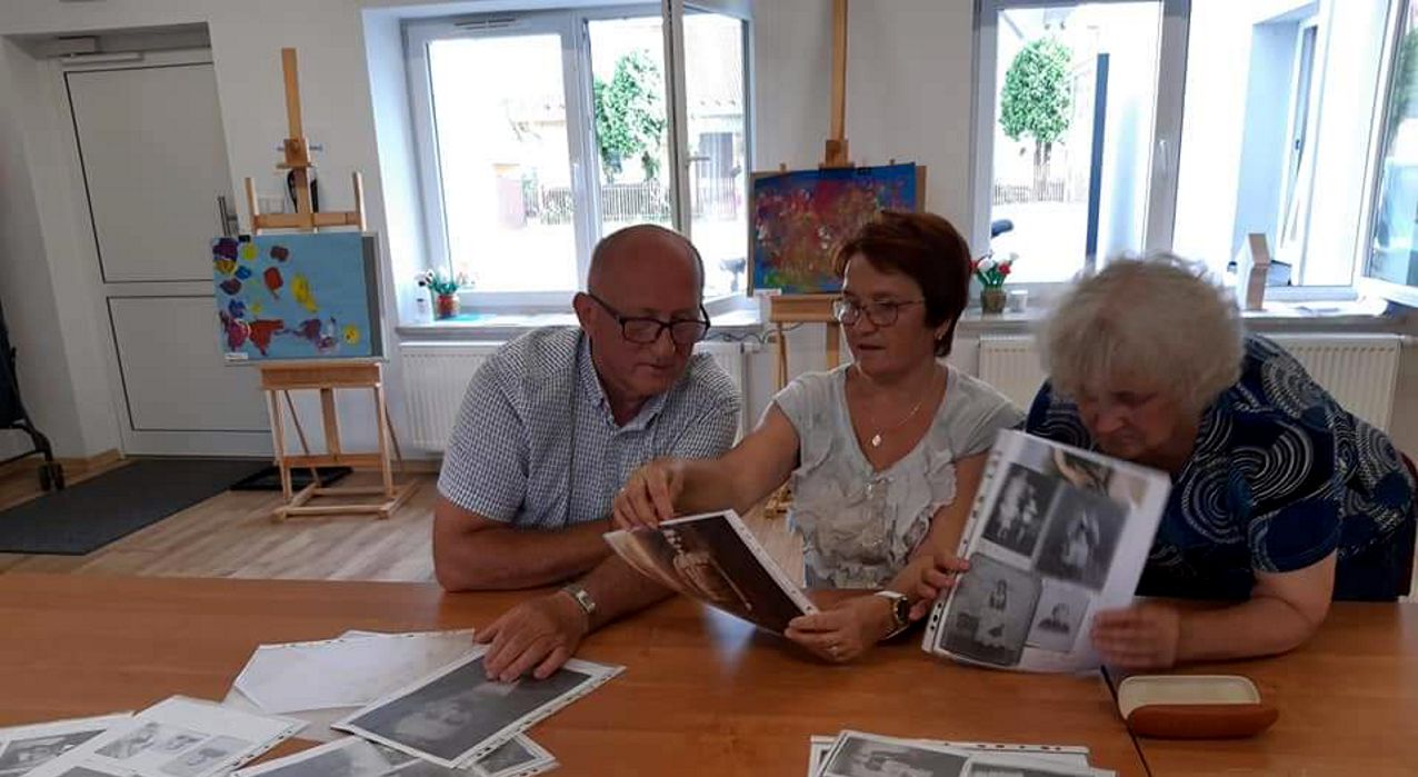 mężczyzna i dwie kobiety oglądają zdjęcia przy stole
