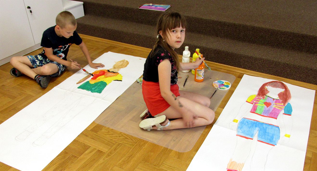 dwoje dzieci projektuje stroje na dużych kartkach malując farbami 