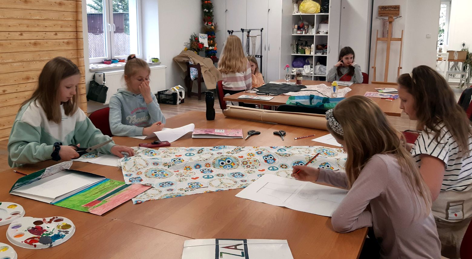 grupa dziewcząt przy dużym stole projektuje na kartkach